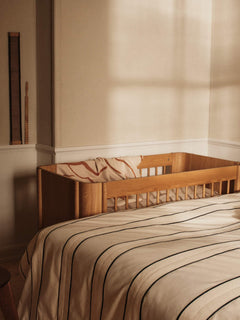 Skye blanket in Sienna/Parchment draped inside an oak cot in a sunlit bedroom
