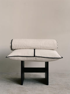 Vari quilted bedspread folded and rolled on a black wooden bench