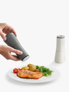 Charcoal Milltop mill grinding over a plate of salmon, with the light grey mill behind