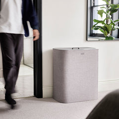 Grey Tota Trio laundry basket standing against a wall in a hallway