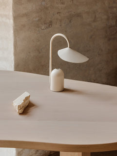 Cashmere Arum Portable Lamp lit on a pale wooden dining table