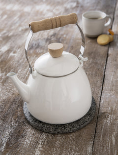 White enamel stove kettle on a stone trivet on a weathered wooden table
