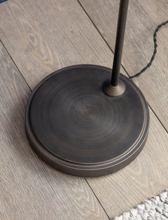 Detail of the weighted antique bronze disc base of the Hoxton Dome floor lamp on a wooden floor