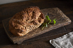 Kaveeta serving board used to present a loaf of seeded bread with fresh herbs