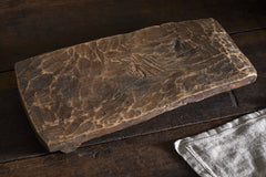 Kaveeta reclaimed wood serving board on a dark wooden table beside a linen cloth