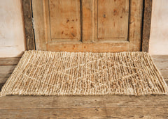 Nkuku Vandi natural jute doormat placed on floorboards in front of a wooden door