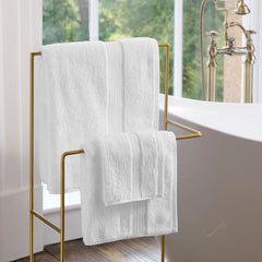 White Christy Supreme towels hanging on a brass rail beside a roll-top bath