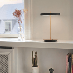 Black Asteria Move portable lamp lit on a bright windowsill
