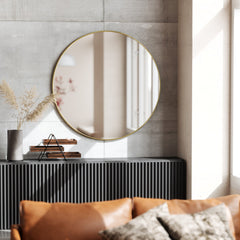 Brass Umbra Hubba round mirror hung above a dark sideboard in a sunlit living room