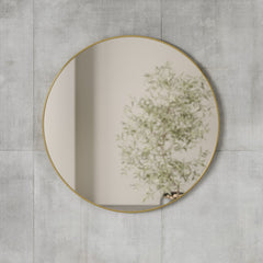 Close view of the brass Umbra Hubba mirror mounted on a pale concrete wall