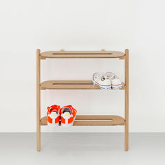 Oak Heel Bar shoe rack leaning against a pale wall holding two pairs of trainers