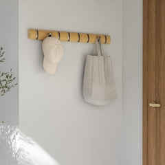 Umbra Flip 8 hook rail in natural wood mounted by a doorway with a cap and towel hung on it