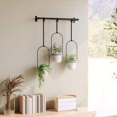 Umbra Triflora planters hung on a pale wall above a shelf of books
